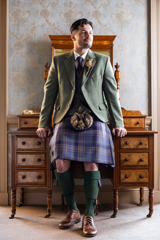 A manis wearing a traditional Highlandwear Outfit of Highland Mist Tartan Kilt, Lovat Mill Green Tweed Jacket and Waistcoat, with traditional sporran, sgian dubh , kiltpin and accessories by Gordon Nicolson Kiltmakers. Laura A Tiliman Photography for YSW