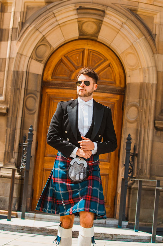 A man is walking in front of McEwan Hall wearing a University of edinburgh Tartan Kilt and formal Prince Charlie Jacket
